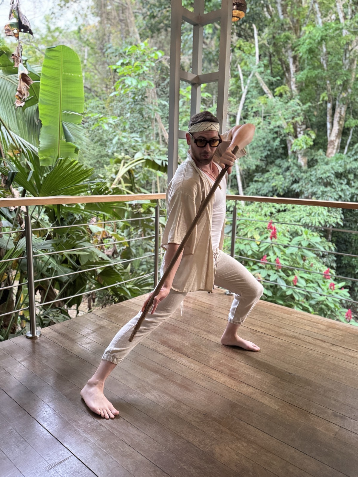 A participant practising a wide stance with a wooden staff on the forest deck