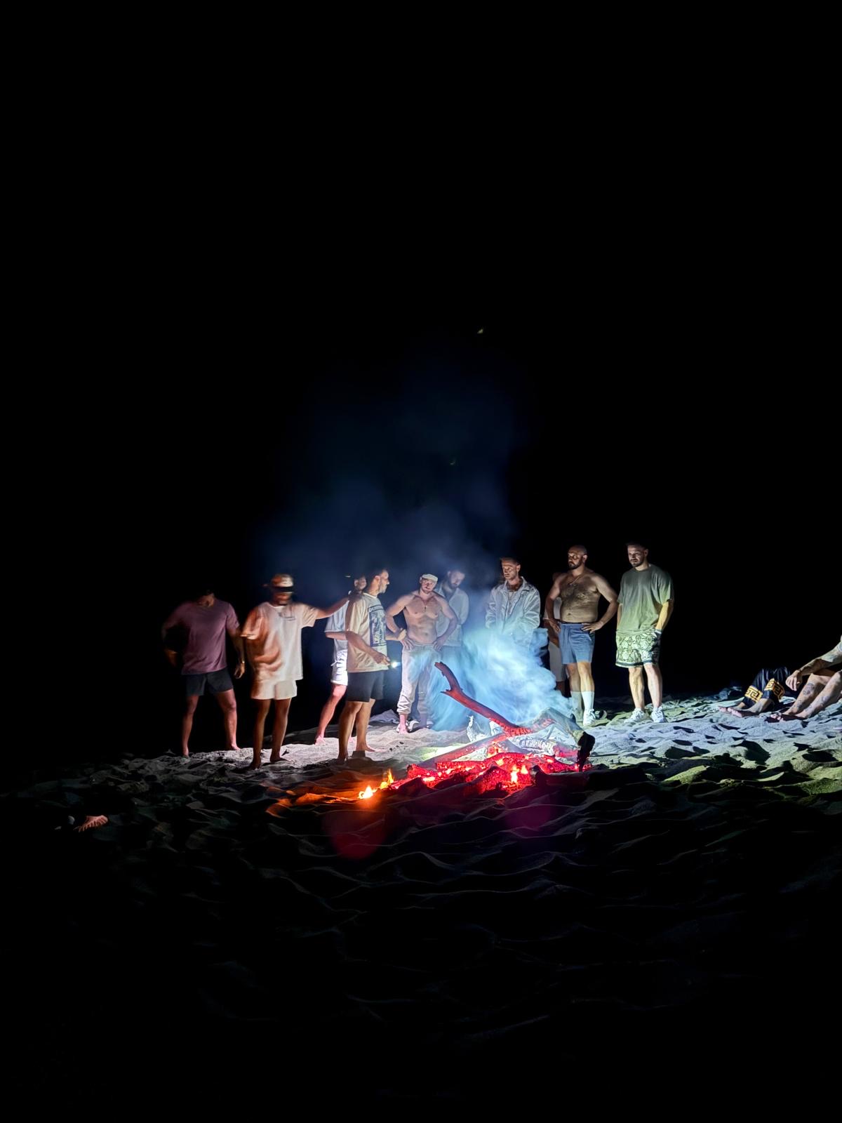 Guests gathered around a beach fire after dark.