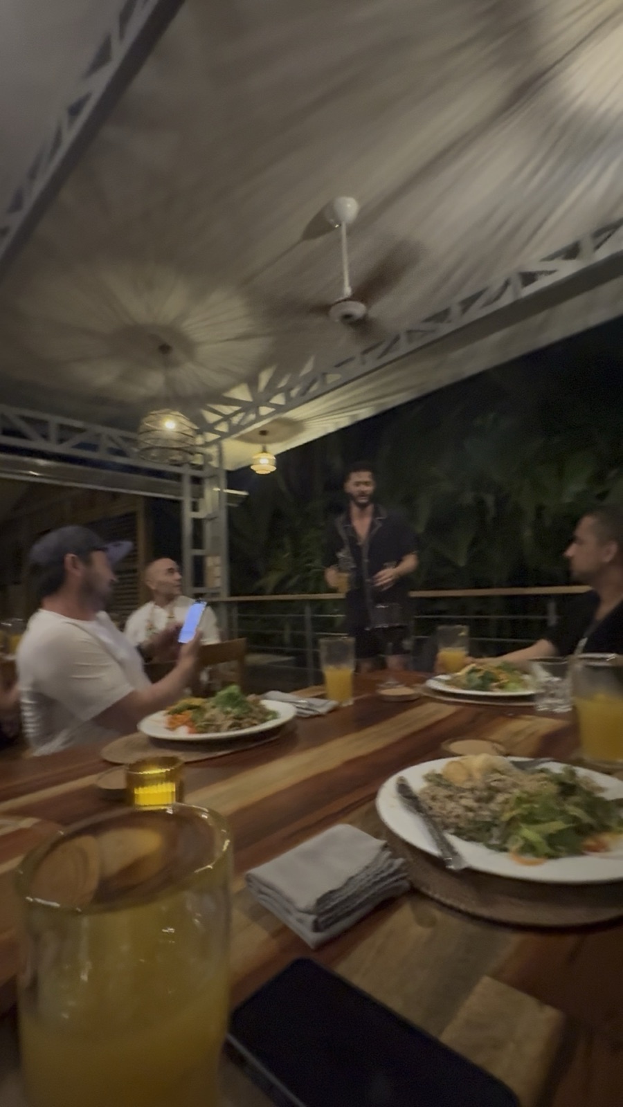 Guests sharing a meal around a wooden table on a covered terrace.