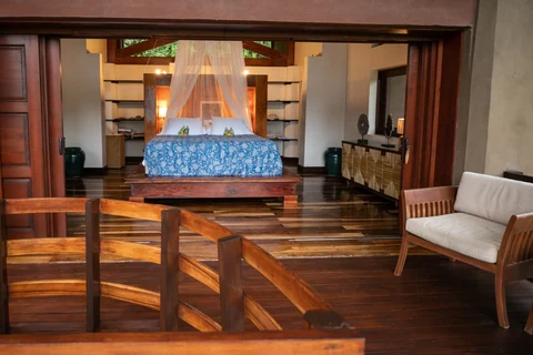 A wide view from the timber terrace into the master bedroom with its blue-covered canopy bed.
