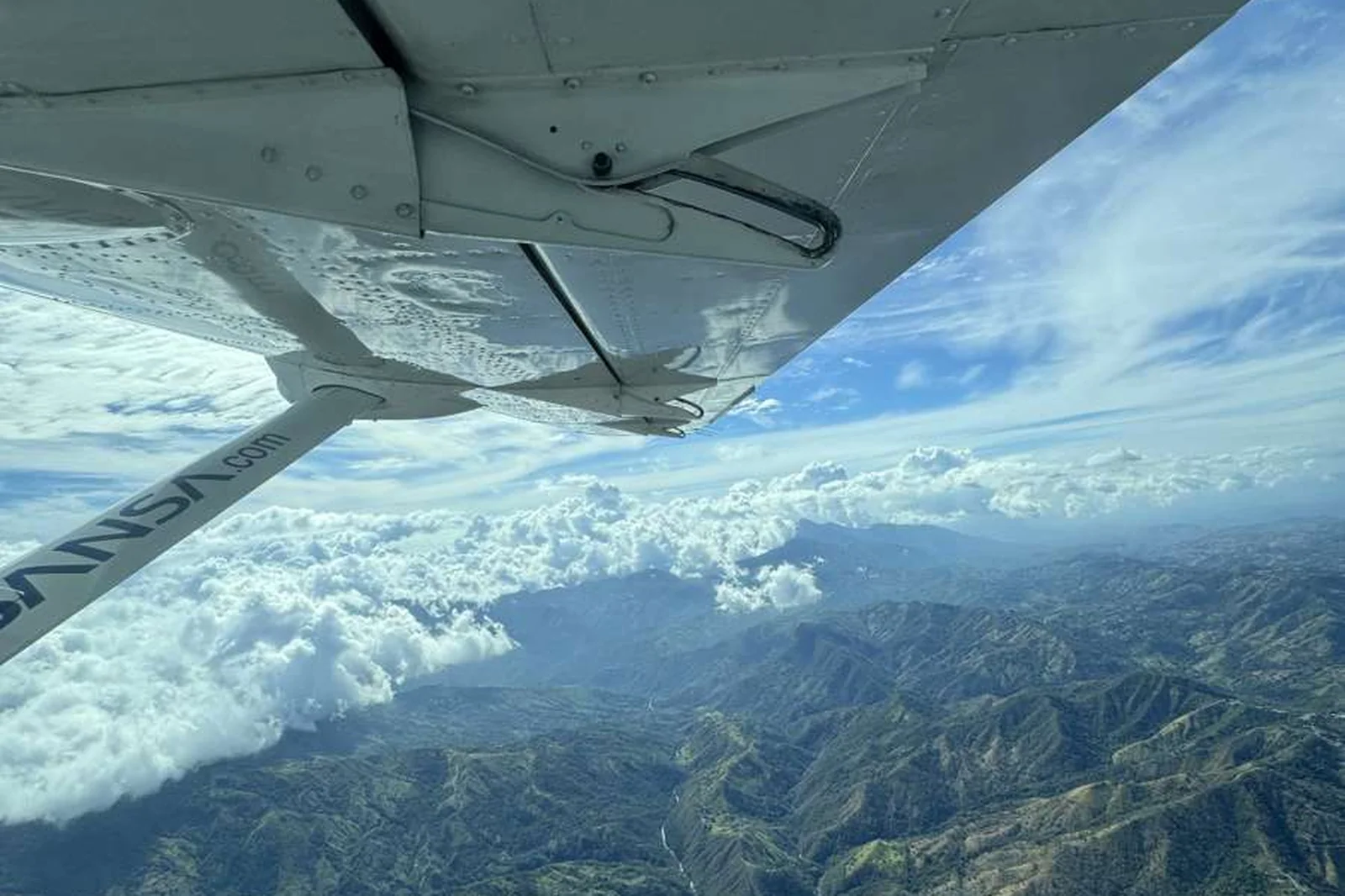 Mountain ranges and clouds beneath the wing of a small plane.