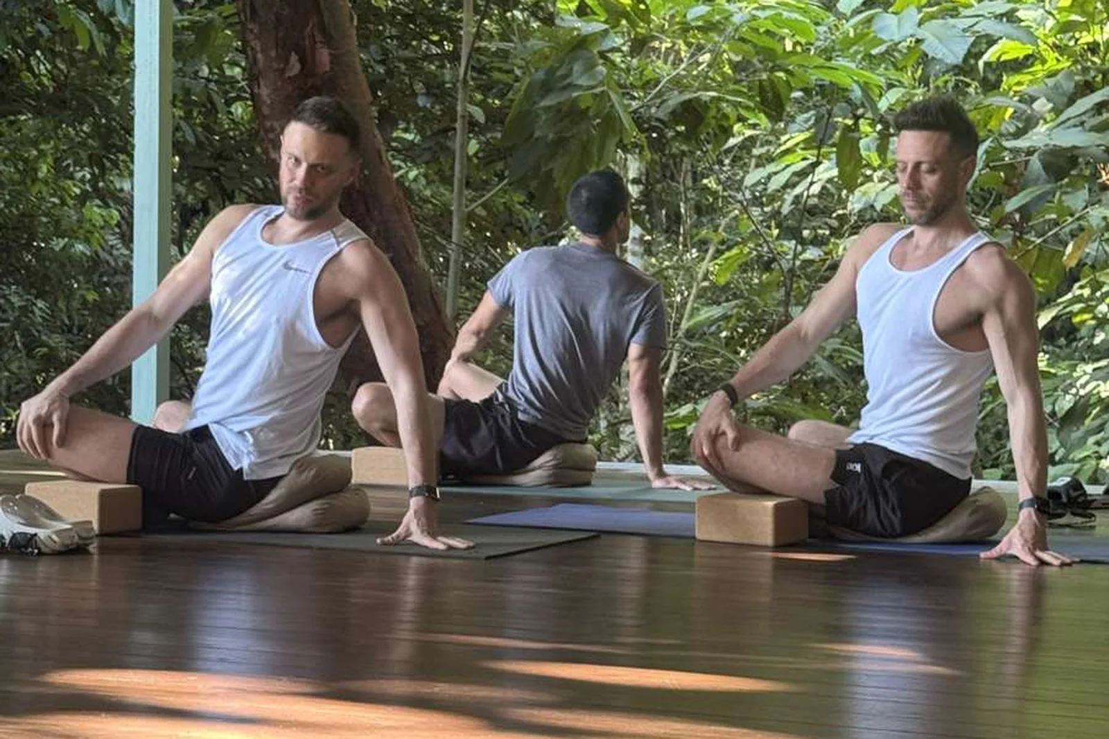 Guests seated on yoga mats on a covered deck surrounded by trees.